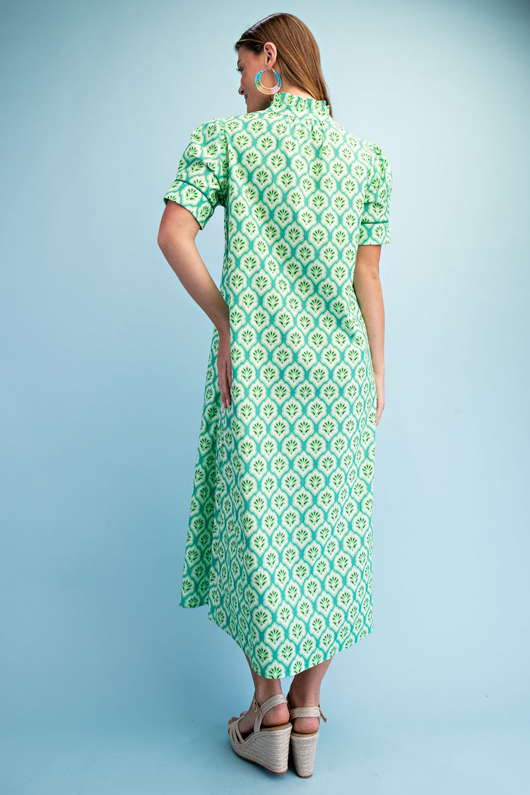 Back view of a woman wearing a green and white printed midi dress with a ruffled collar.