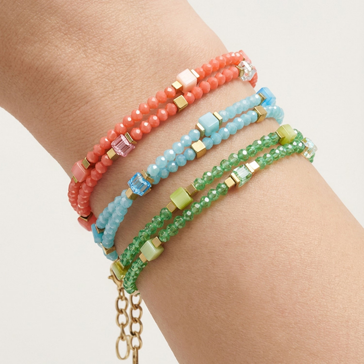 Three Joyful Colours Flex bracelets in coral, blue, and green on a wrist with gold cube accents.