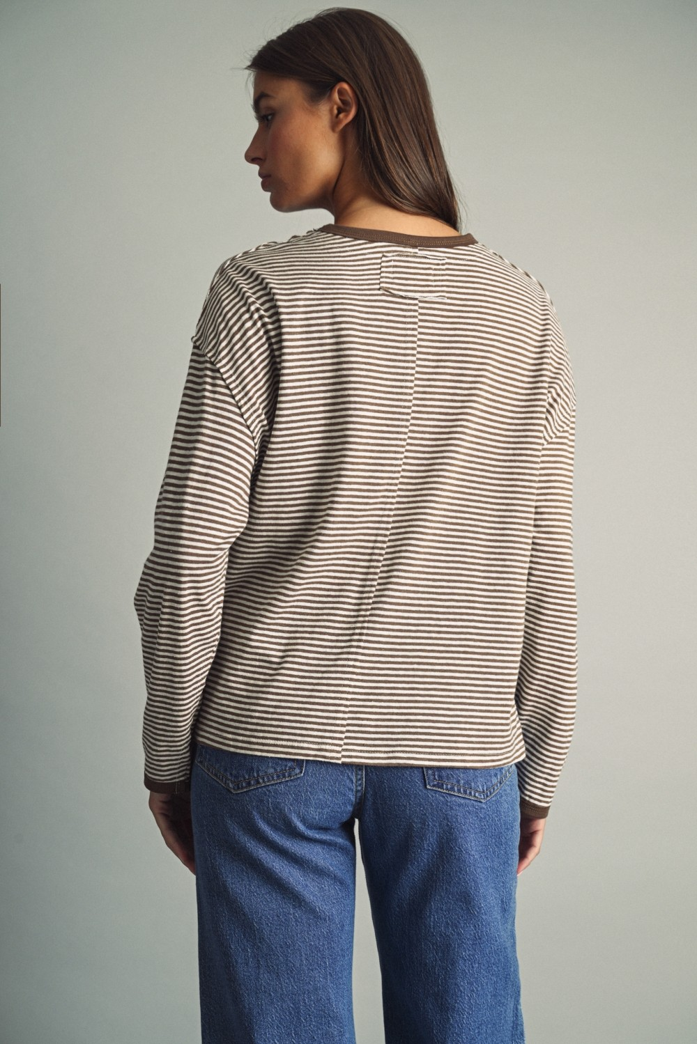 Back view of a woman in a brown and white thin striped long sleeve top with blue jeans.
