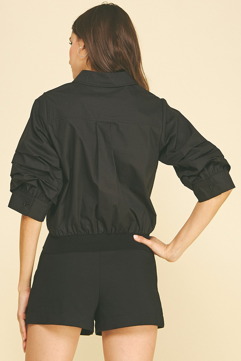 Back view of a woman wearing a black Jaycee cropped shirt with pleated sleeves and a banded hem.