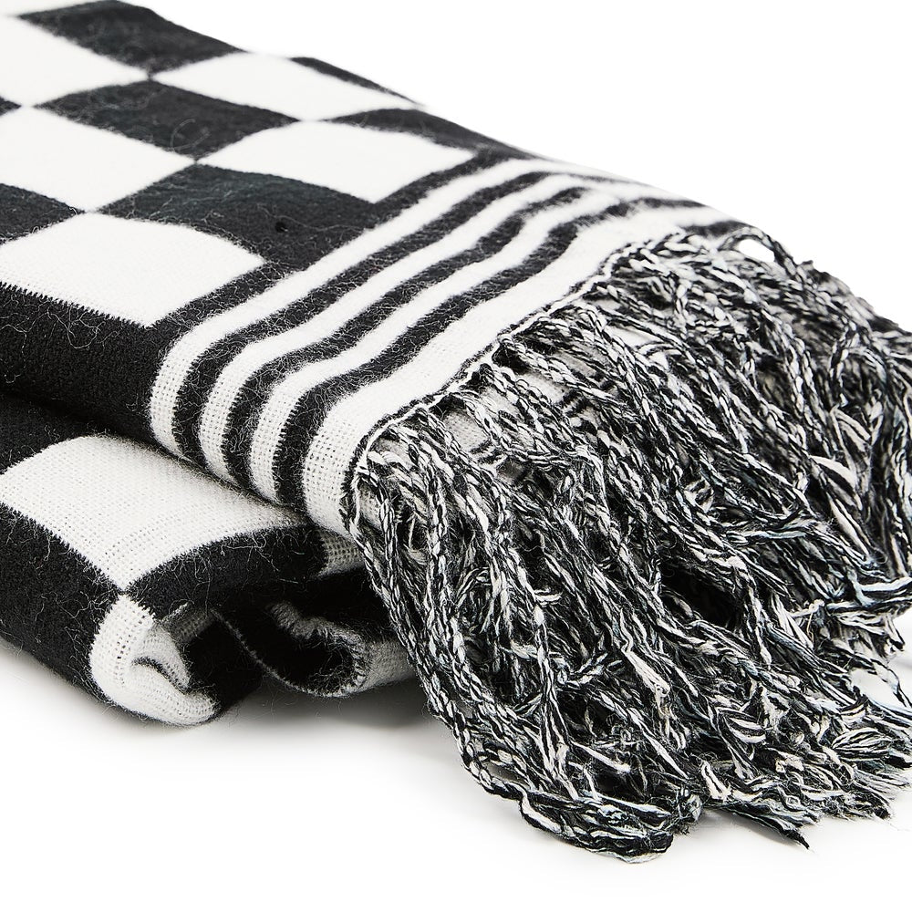Close-up of a folded black and white checkered acrylic throw blanket with striped edge and fringe.