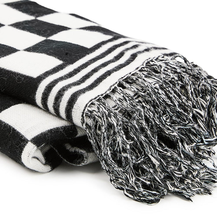 Close-up of a folded black and white checkered acrylic throw blanket with striped edge and fringe.