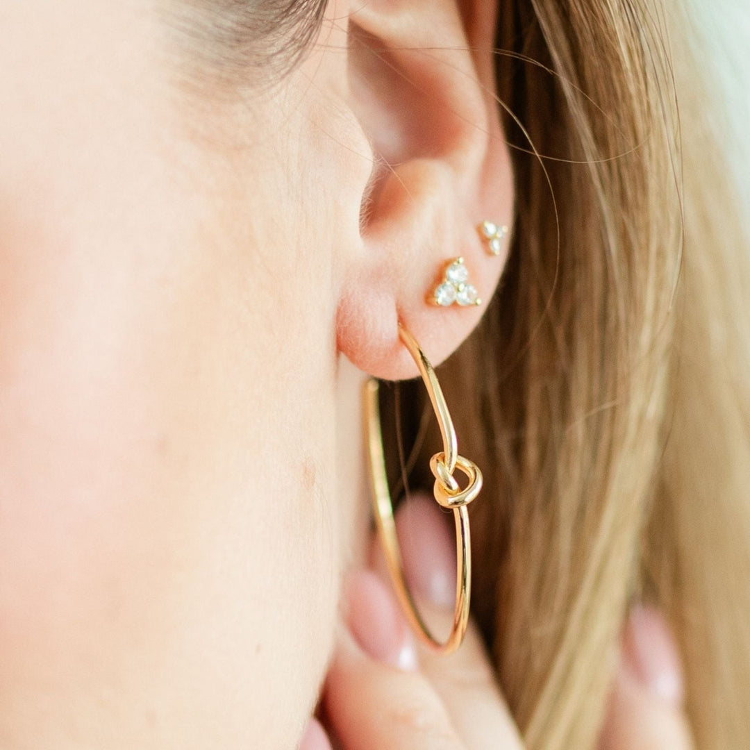 Close-up of a person wearing gold-colored delicate knot hoop earrings with a 1.5-inch drop.