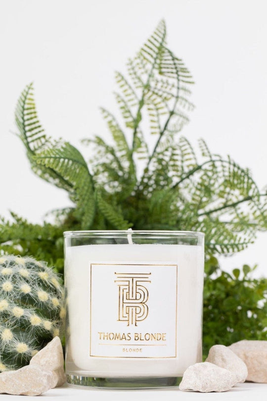 Thomas Blonde signature scent candle in a clear glass jar with a white label and gold logo.