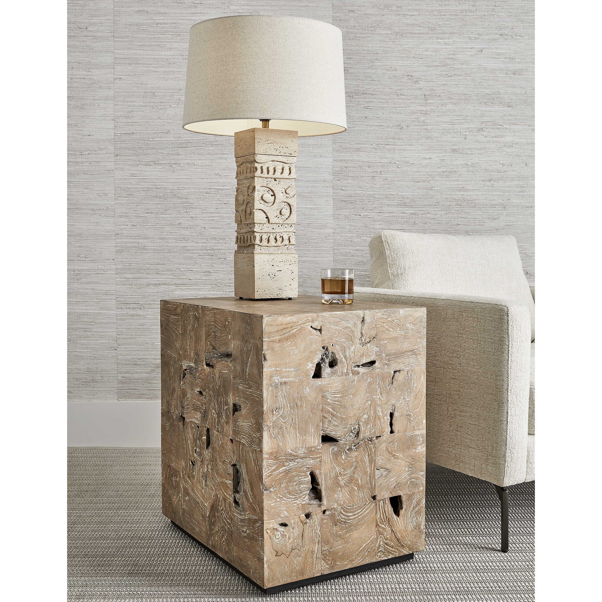 A rustic wooden cube end table with a textured stone lamp and a glass of whiskey.