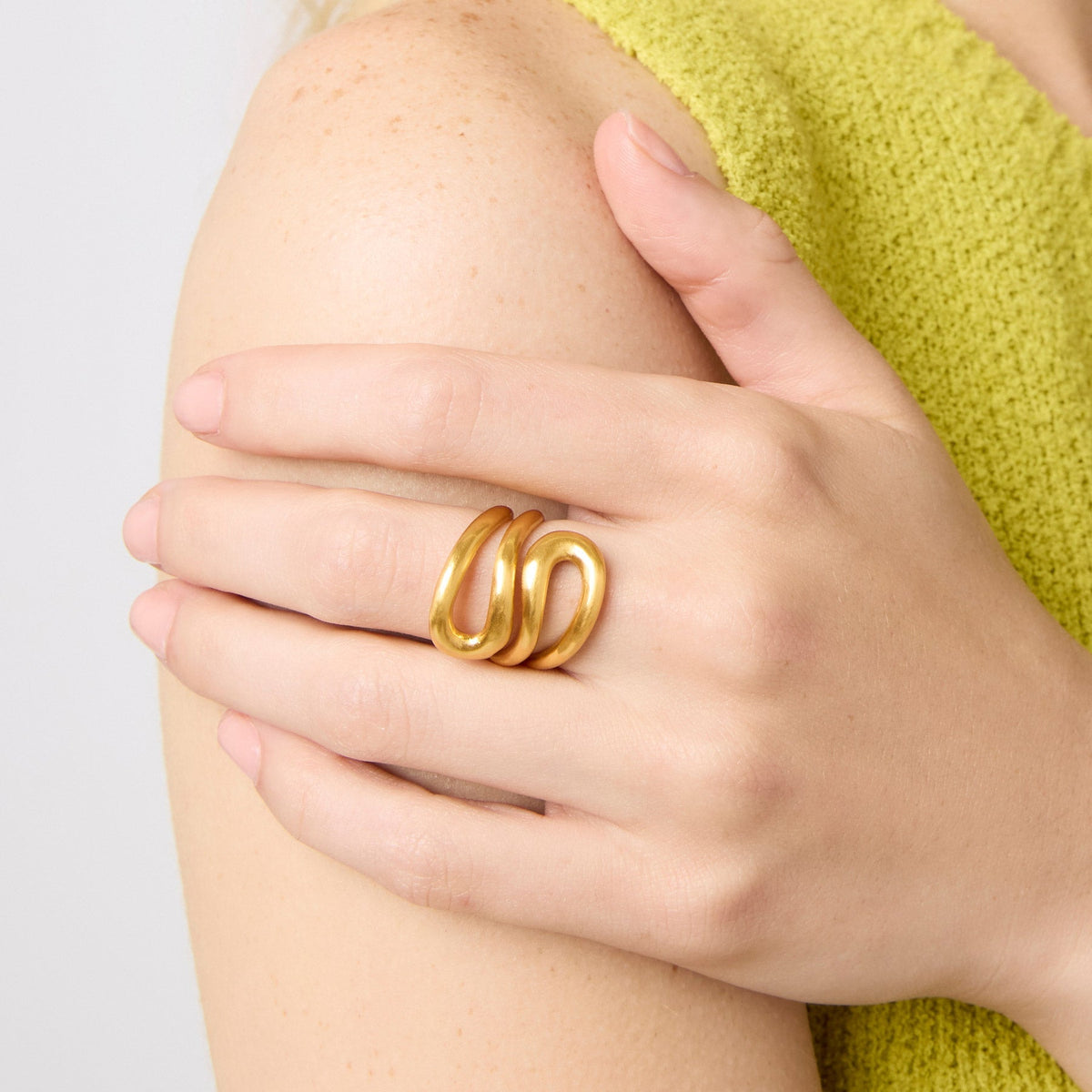 A person wearing a Wave Wrap Ring in 24K gold plate on their ring finger.