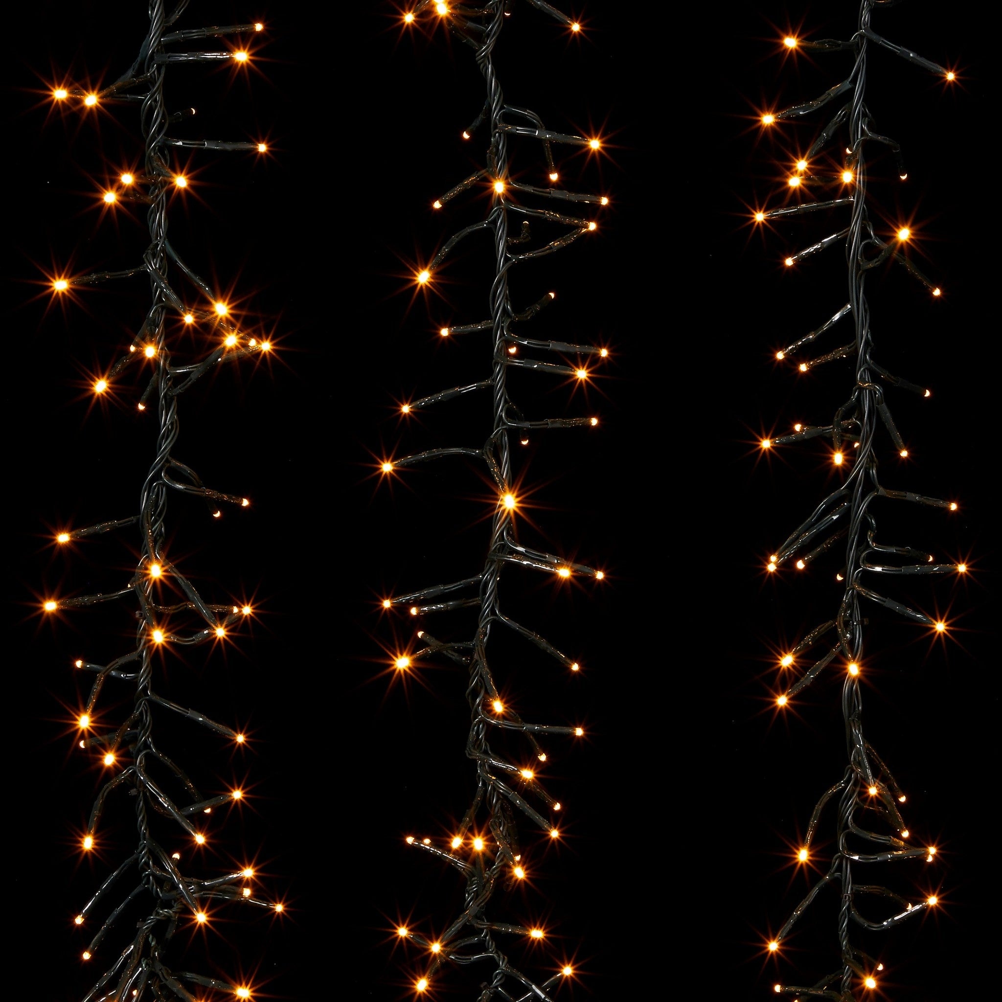 Three strands of warm white LED cluster lights on dark green wire against a black background.