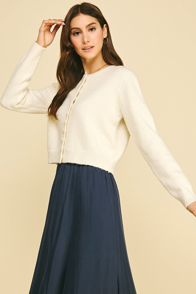 Woman wearing a cream crystal button down long sleeve cardigan with a navy blue skirt.