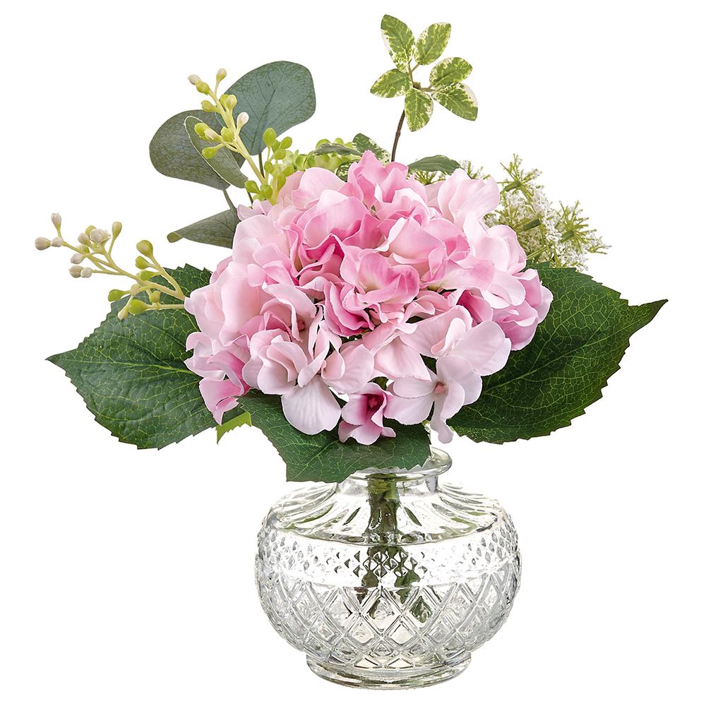 Glass vase holding artificial hydrangea flowers with green foliage.