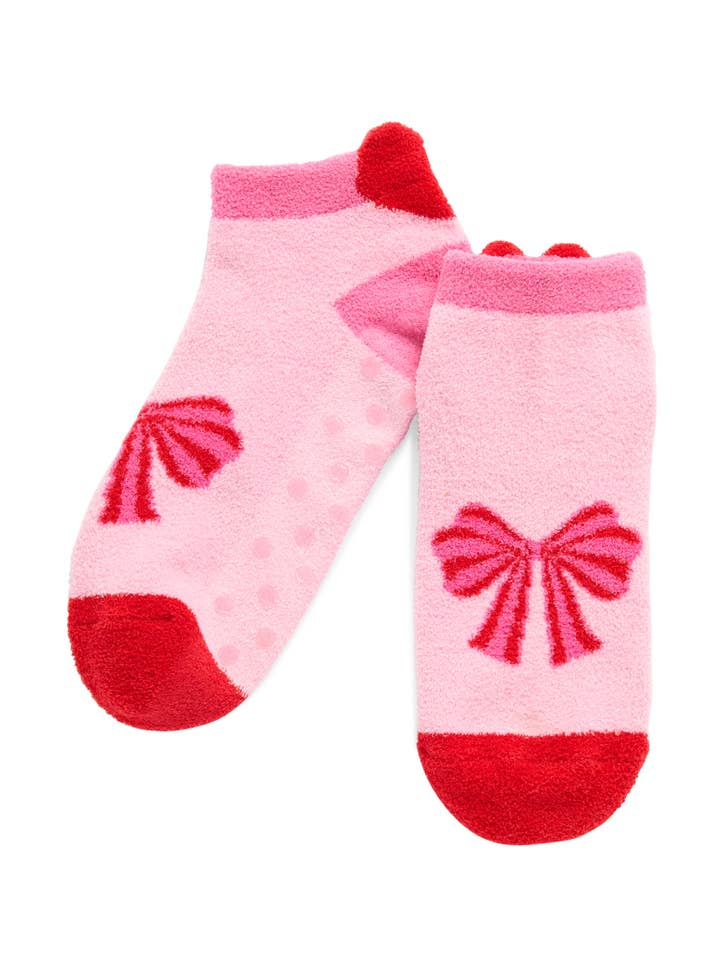 Pair of pink fuzzy low-cut home socks featuring red bow designs and red toe and heel accents.