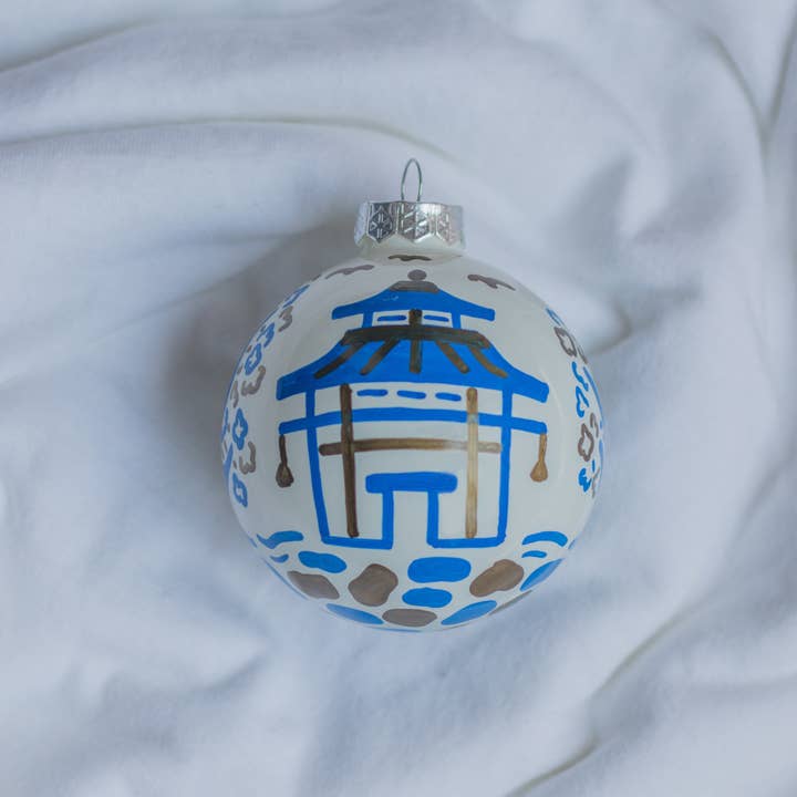 Hand-painted pagoda scene ornament in red with gold accents on a white ceramic sphere.