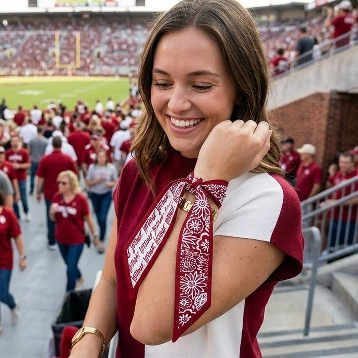 Woman wearing a maroon and white Oklahoma Sooners skinny scarf tied around her wrist at a stadium.