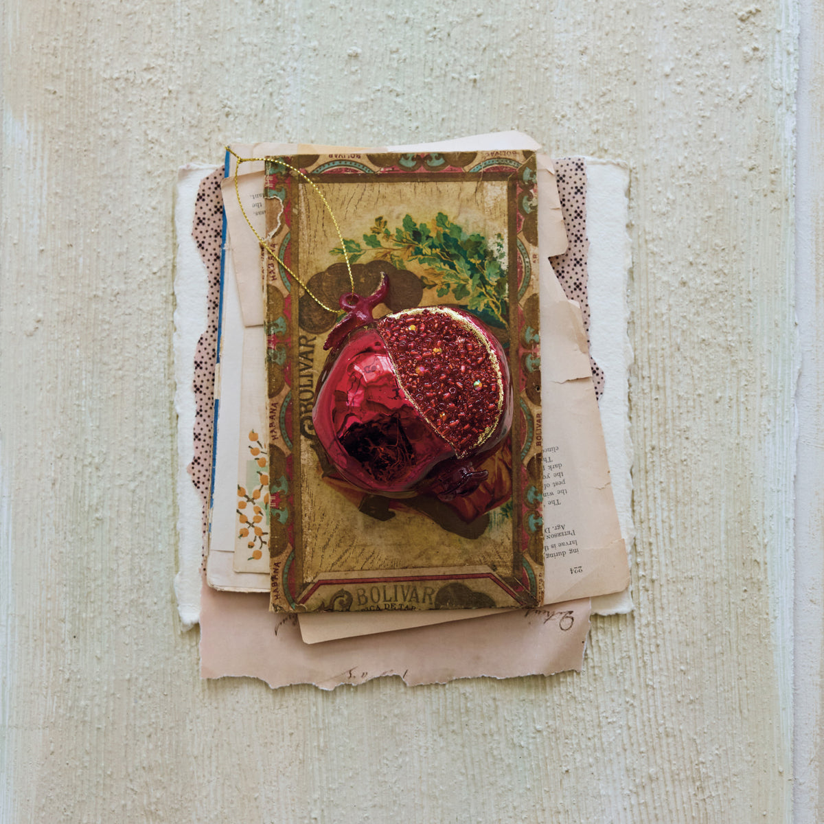 Hand-painted red mercury glass pomegranate ornament with gold beads on vintage paper background.