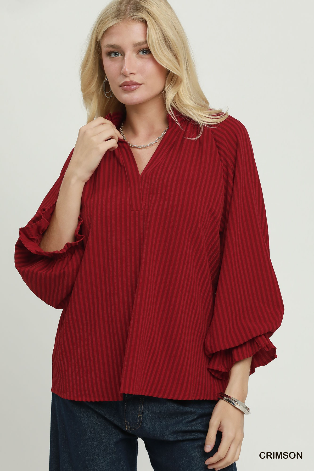 Woman wearing a crimson Emma Stripe Split Neck Blouse with a ruffle collar and long puff sleeves.