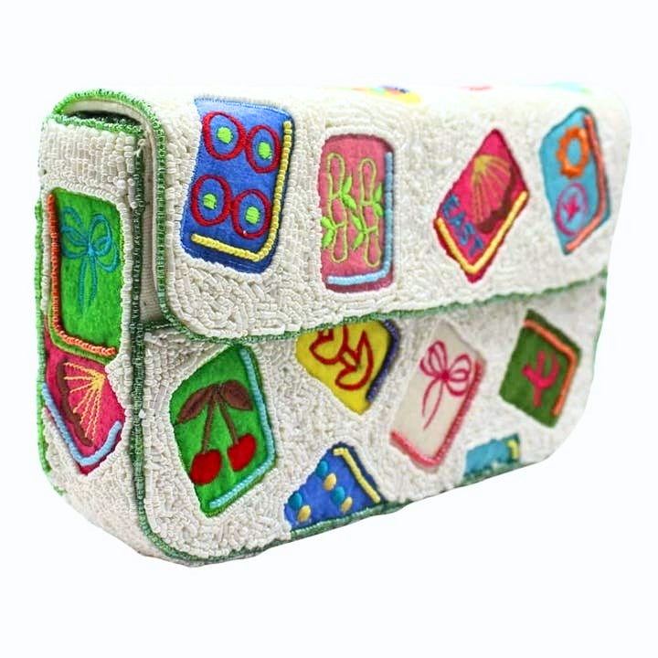 White beaded shoulder bag with colorful embroidered mahjong tile motifs and a front flap closure.