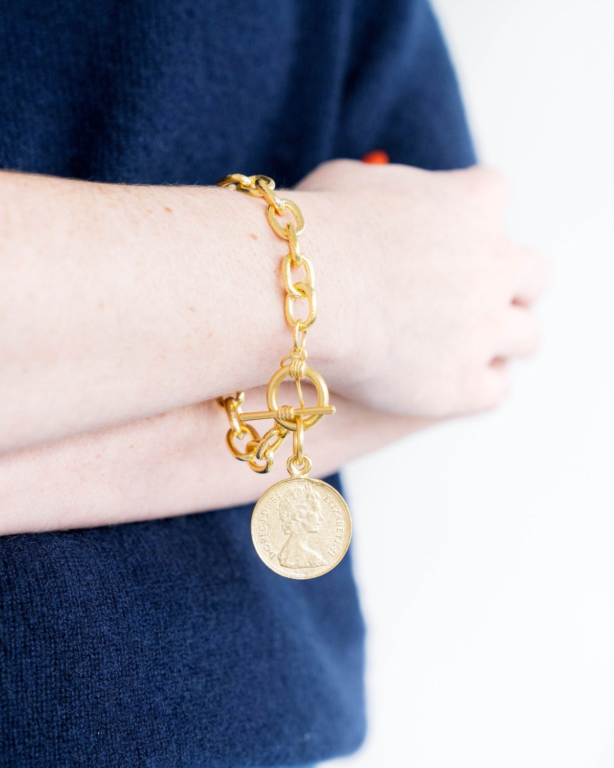 Gold chain bracelet with a Queen Elizabeth II coin pendant and toggle clasp on a person's wrist.