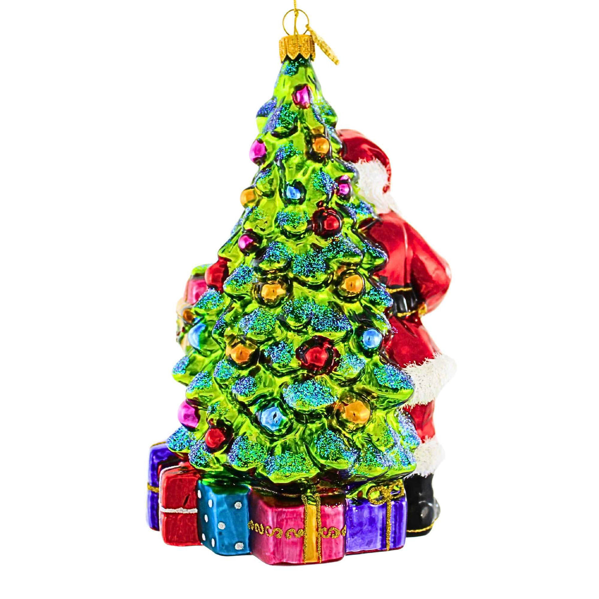 Glass Christmas ornament of Santa Claus standing behind a decorated tree with gifts at the base.
