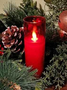 Red glass LED pillar candle, 2x5 inches, surrounded by pine branches and holiday decor.
