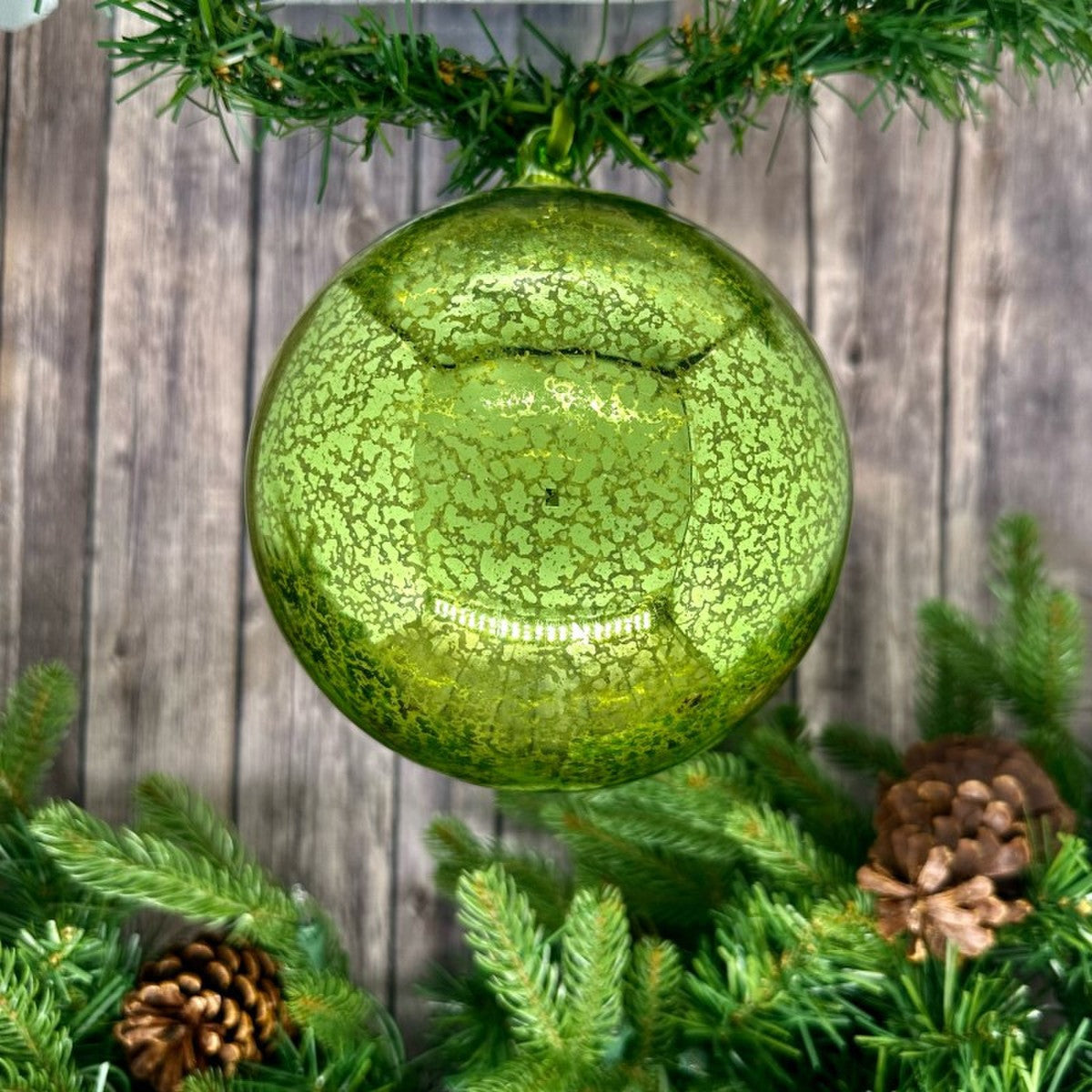 Green hand-blown mercury glass ornament with a vintage speckled finish hanging from a garland.