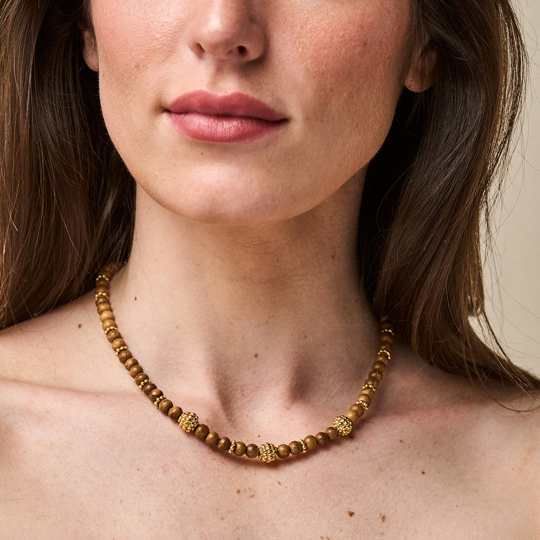 Woman wearing a Berry Single Strand Petite Beads Necklace with wooden beads and gold berry motifs.
