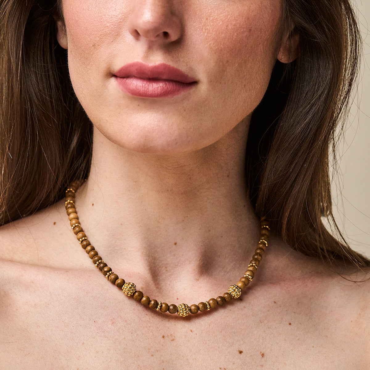 Woman wearing a Berry Single Strand Petite Beads Necklace with wooden beads and gold berry motifs.