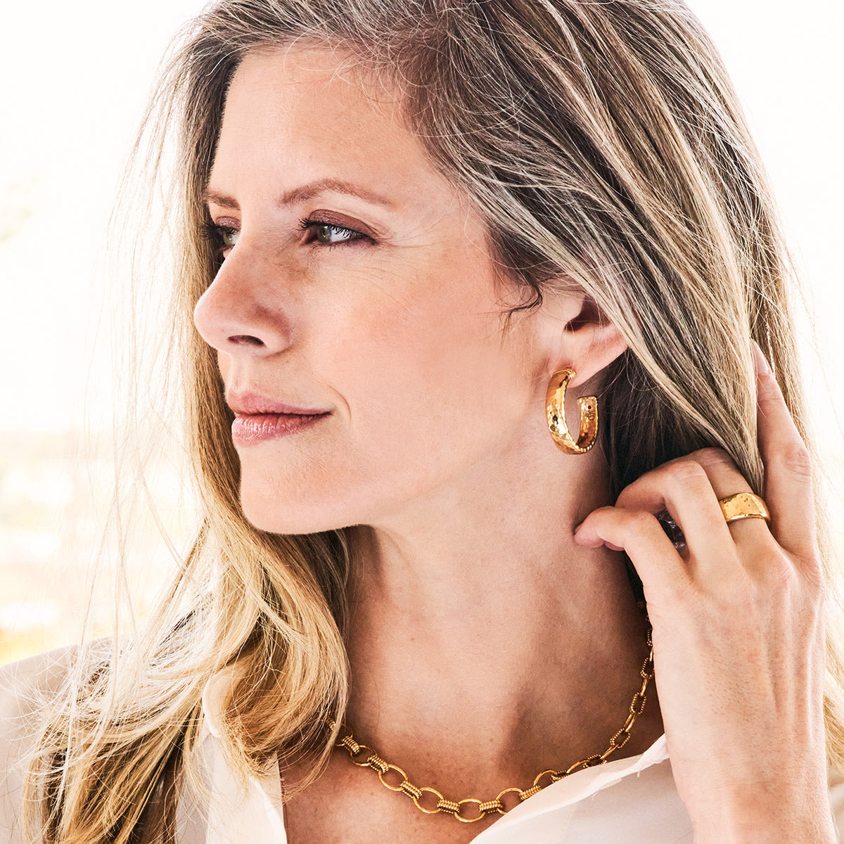 Woman wearing Cleopatra Classic Medium Hoop Earrings in hammered 18K gold over brass.
