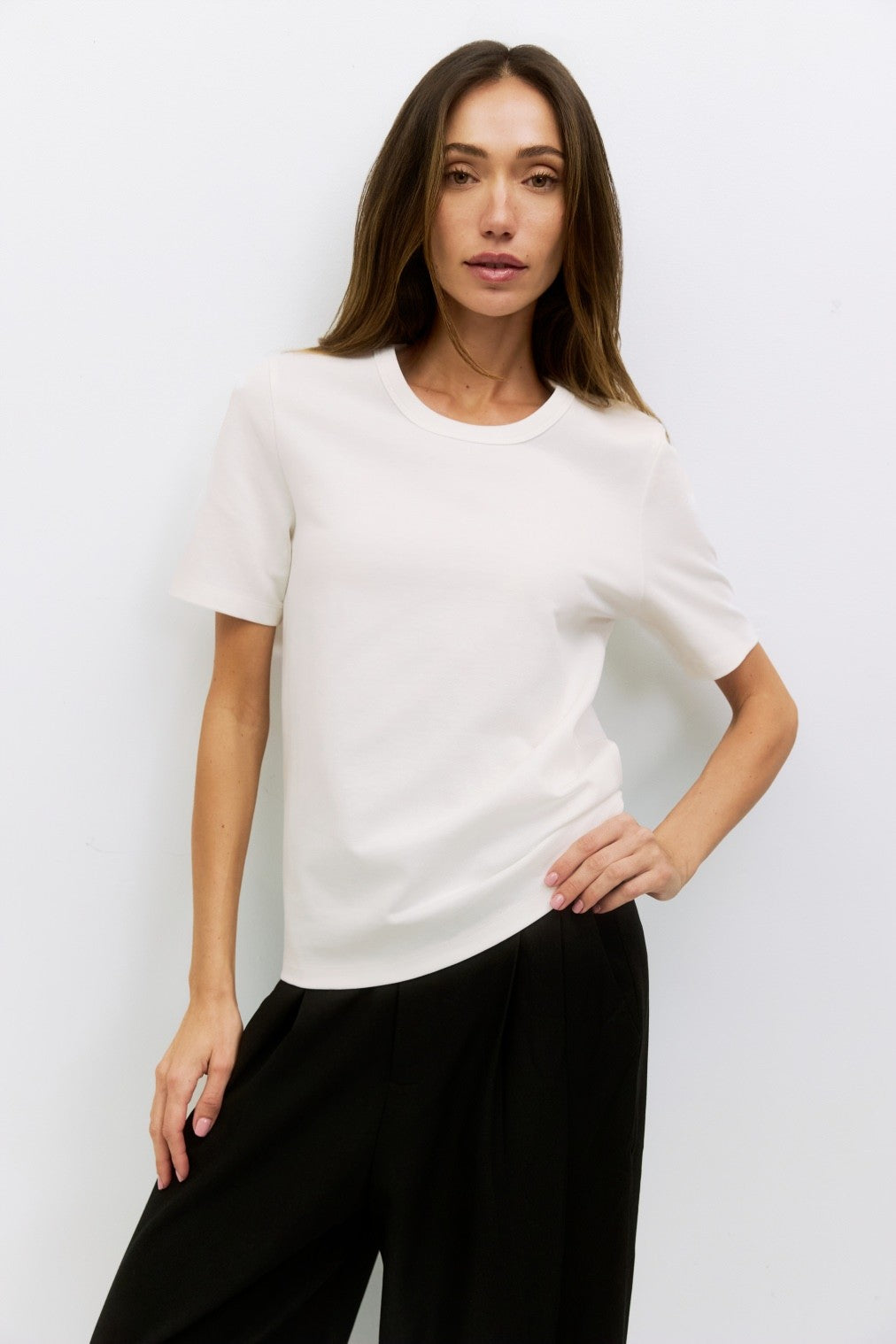 Woman wearing a white crew neck short-sleeve Anita Top made of cotton and nylon, paired with black wide-leg pants.