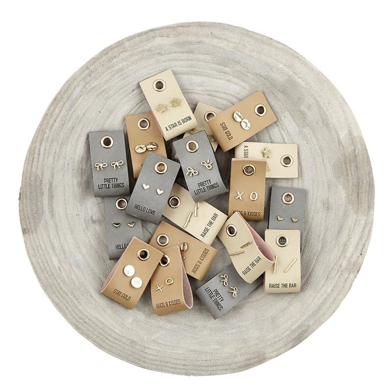 Gold stud earrings stored on a rectangular brown leather tag measuring one inch wide by two inches high.