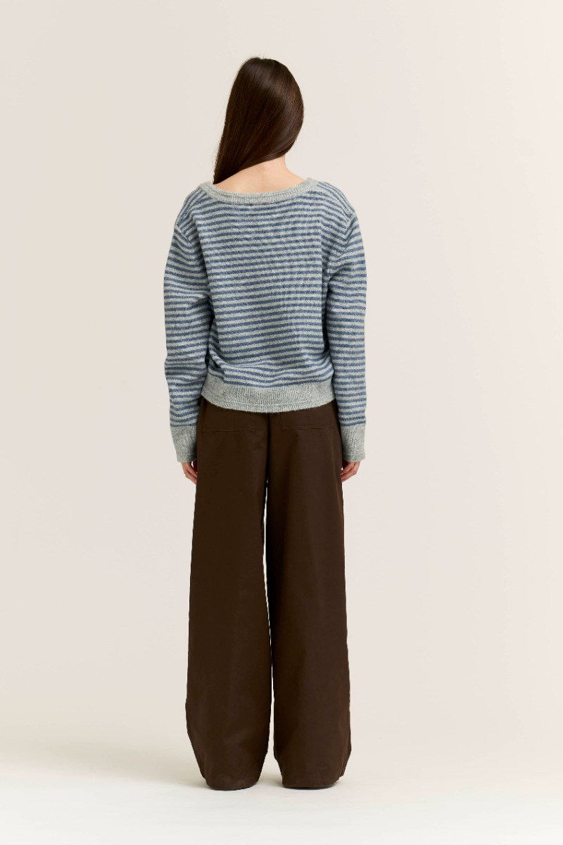 Back view of a woman wearing the Sienna Striped V-Neck Sweater in blue and gray with brown trousers.