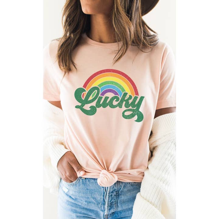 Woman wearing a peach-colored t-shirt with a retro distressed rainbow and green 'Lucky' graphic.