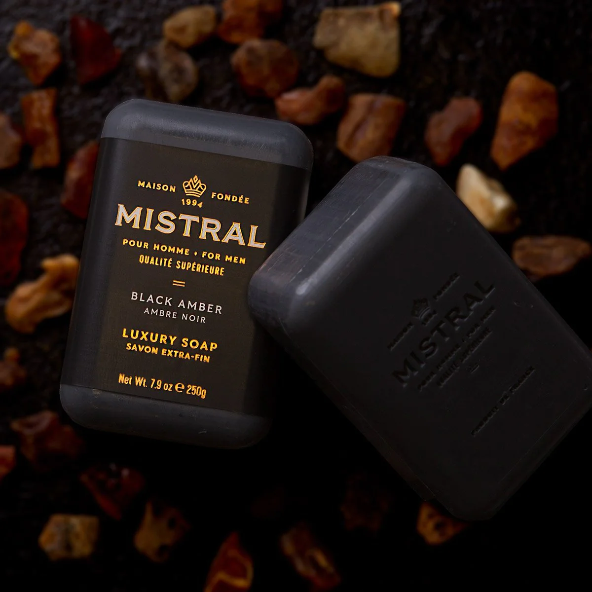 Two bars of Mistral Black Amber soap for men, one in black packaging and one unwrapped.