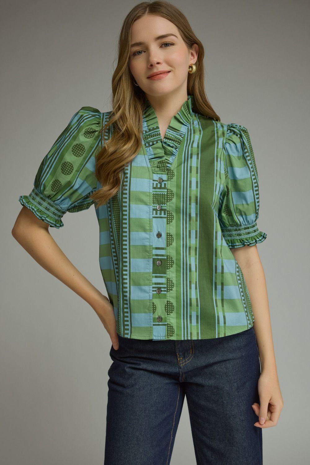 Woman wearing a green and blue mixed print top with ruffle neck and short puff sleeves.