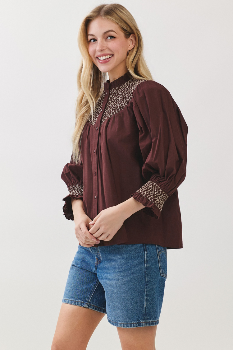 Woman wearing a Jenny Embroidered Button Down Blouse in burgundy with blue denim shorts.