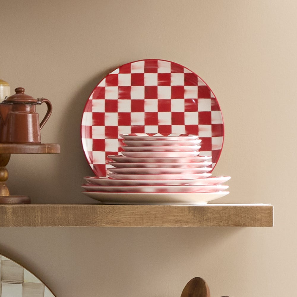 A stack of stoneware dinner plates featuring a red and white hand-painted cherry check pattern.