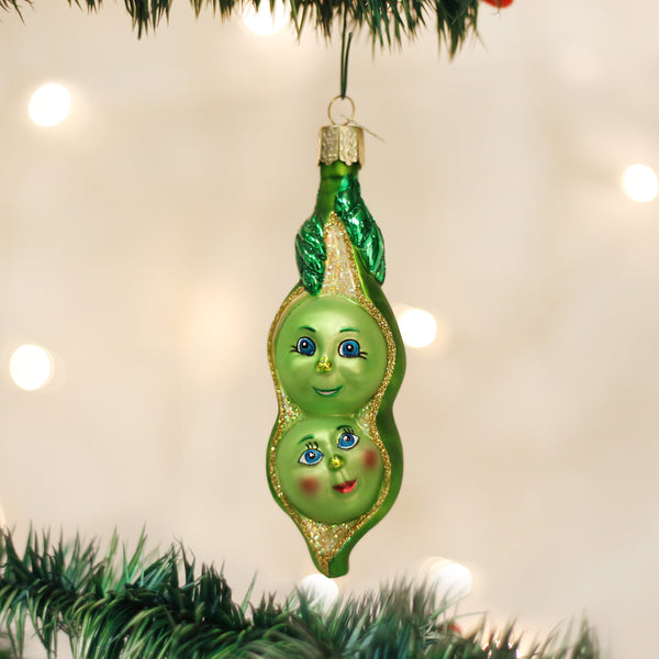 Two Peas In A Pod glass Christmas ornament with hand-painted faces and glitter accents.