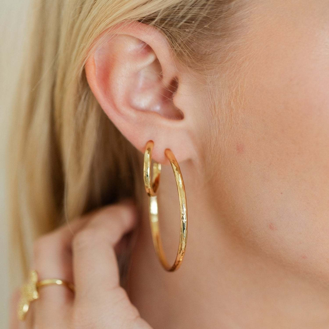 Large delicate hoop earrings with a lightly textured finish in gold.