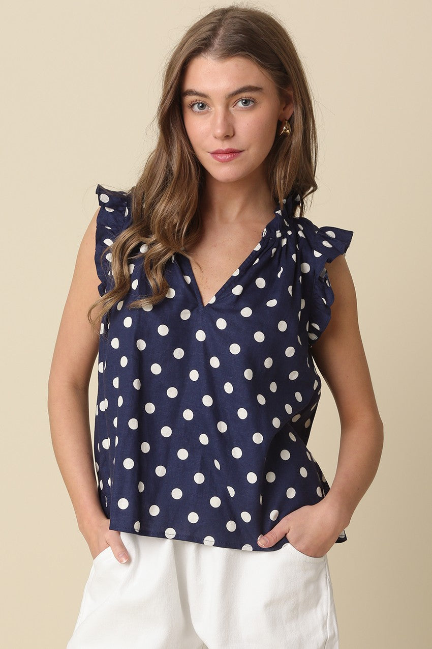 Woman wearing a navy blue Mira Polka Dot Ruffle Blouse with white dots and white pants.