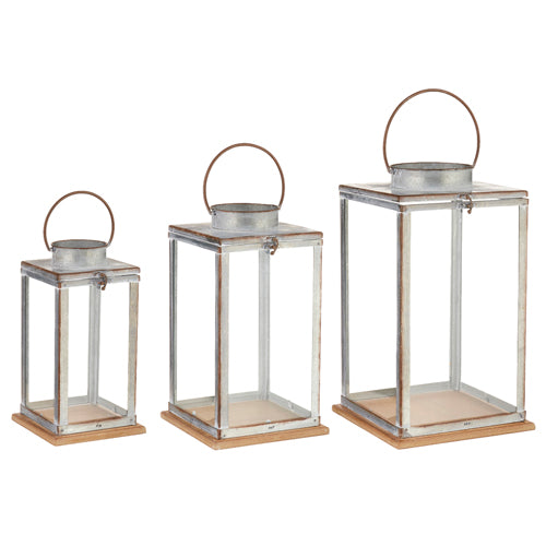 Set of three galvanized metal and glass lanterns with wooden bases in varying sizes.