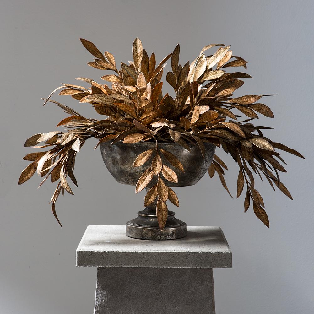 24-inch copper gold bay leaf spray arranged in a dark metallic pedestal bowl on a stone plinth.