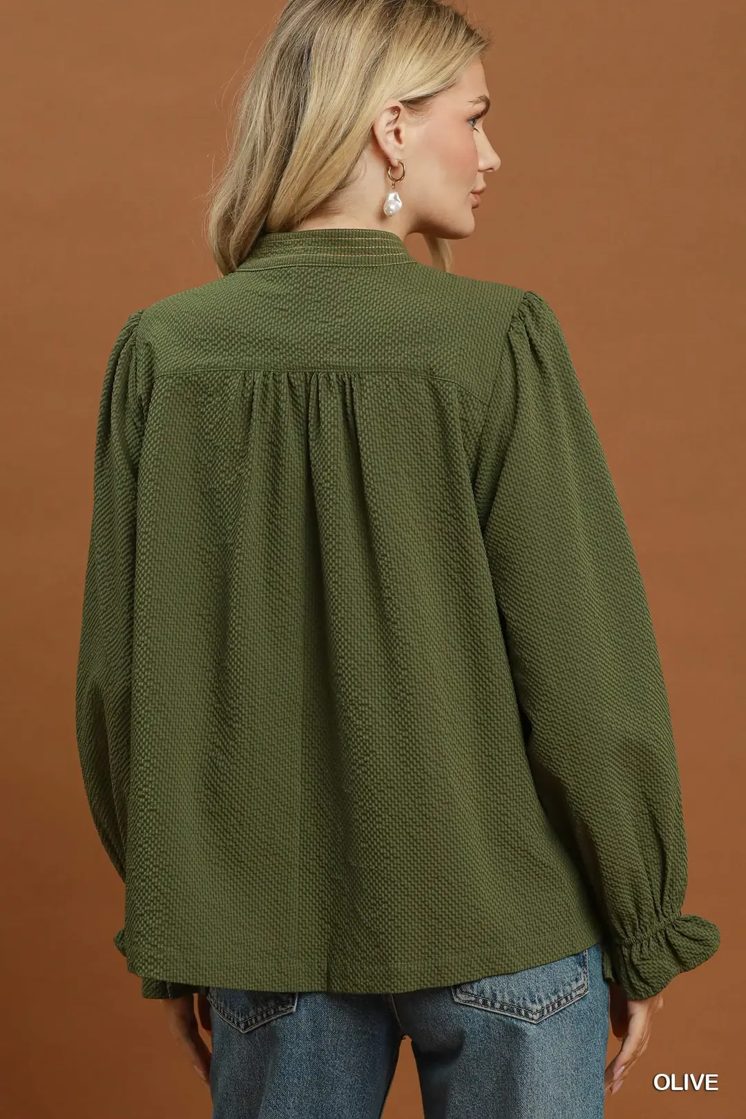 Back view of a woman wearing an olive green textured puff sleeve blouse with blue jeans.