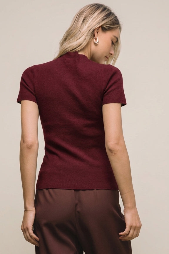 Back view of a woman wearing a burgundy short sleeve mock neck knit sweater top.