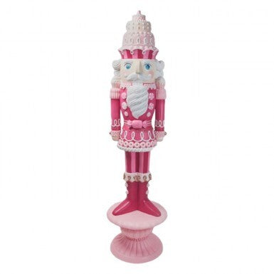 A tall, pink resin nutcracker with white accents, standing on a pink cake plate base.