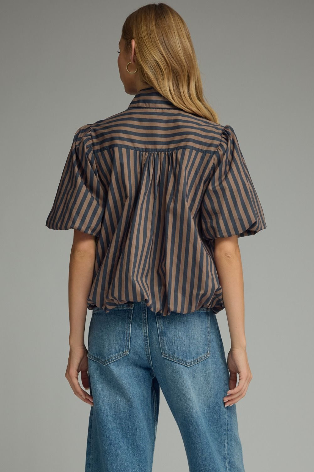 Back view of a woman wearing a brown and navy striped short puff sleeve top with blue jeans.