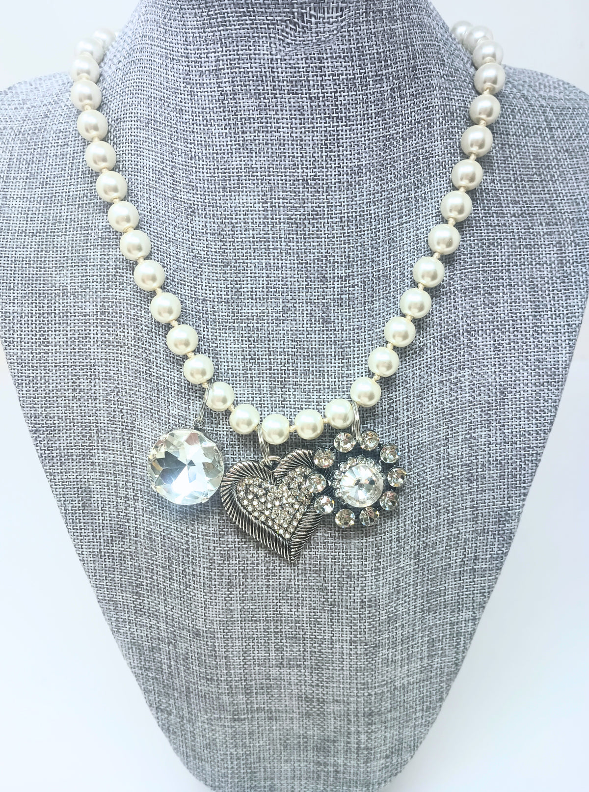 18-inch pearl necklace with three silver-toned charms: a large crystal, a heart, and a floral gem.
