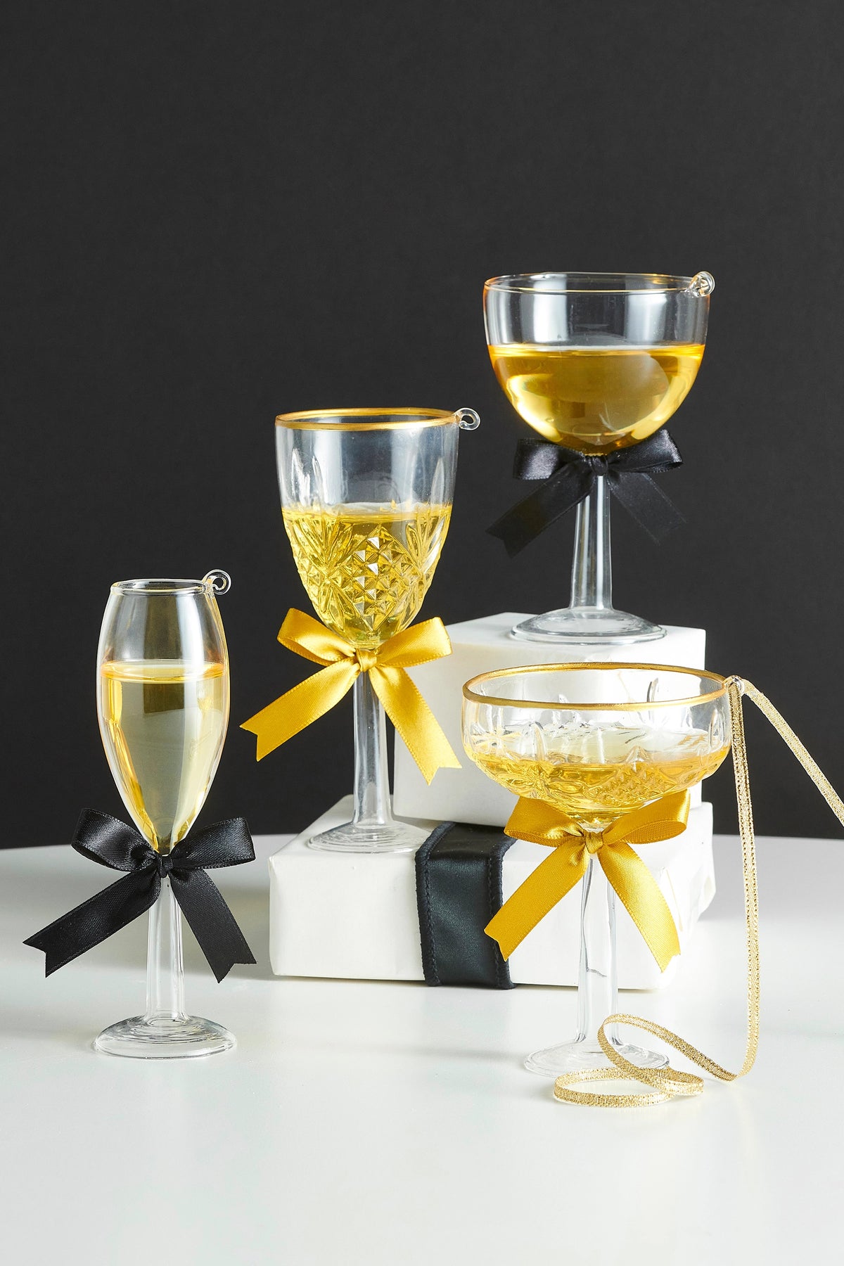 Four assorted glass champagne and wine glass ornaments with gold liquid and decorative bows.