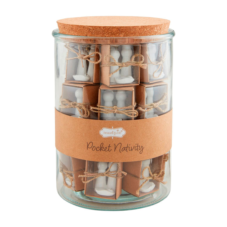 Glass jar filled with individually boxed white dolomite Pocket Nativity sets tied with twine.