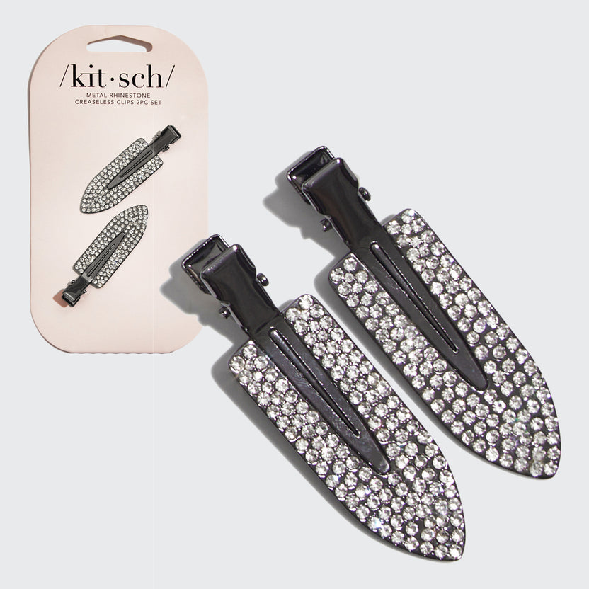 Two black metal creaseless hair clips with clear rhinestone embellishments on a pink card.