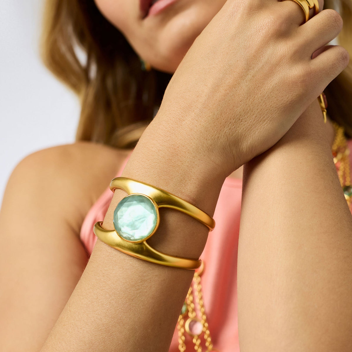 A person wearing the Laguna Stone Cuff, a gold-toned open bracelet with a large round green stone.