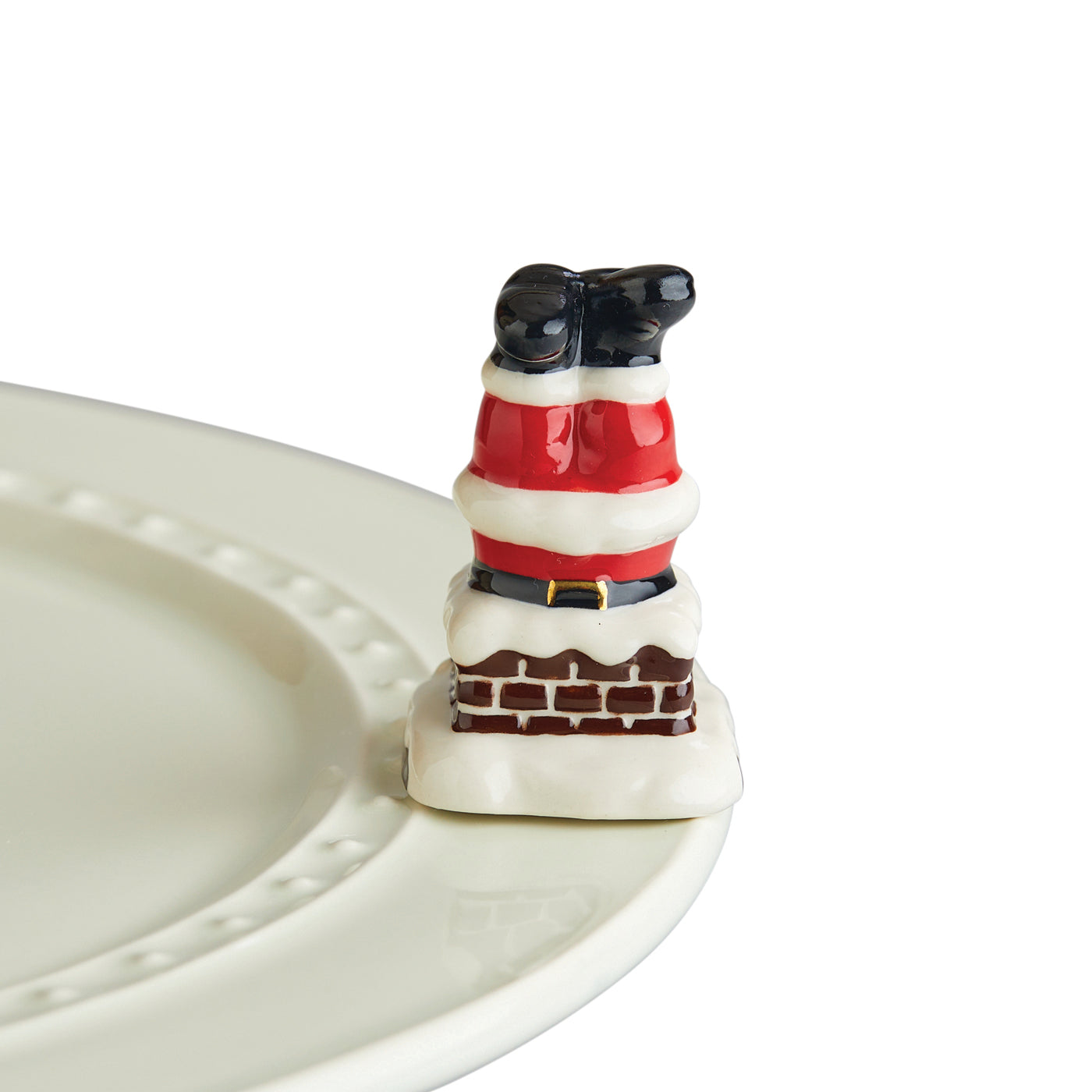 Ceramic Santa's legs stuck in a chimney on a white plate edge.