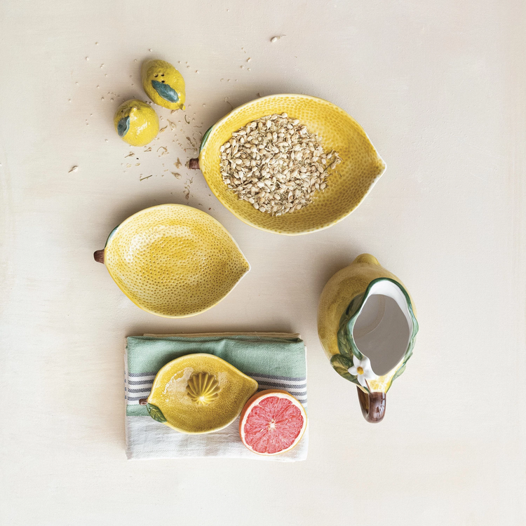 Yellow stoneware lemon-shaped juicer on a striped cloth next to a grapefruit half and lemon dishes.